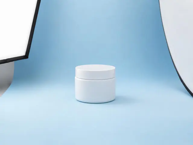Un bote de crema blanco en un pequeño plató de producto con fondo azul claro, un foco y un rebotador